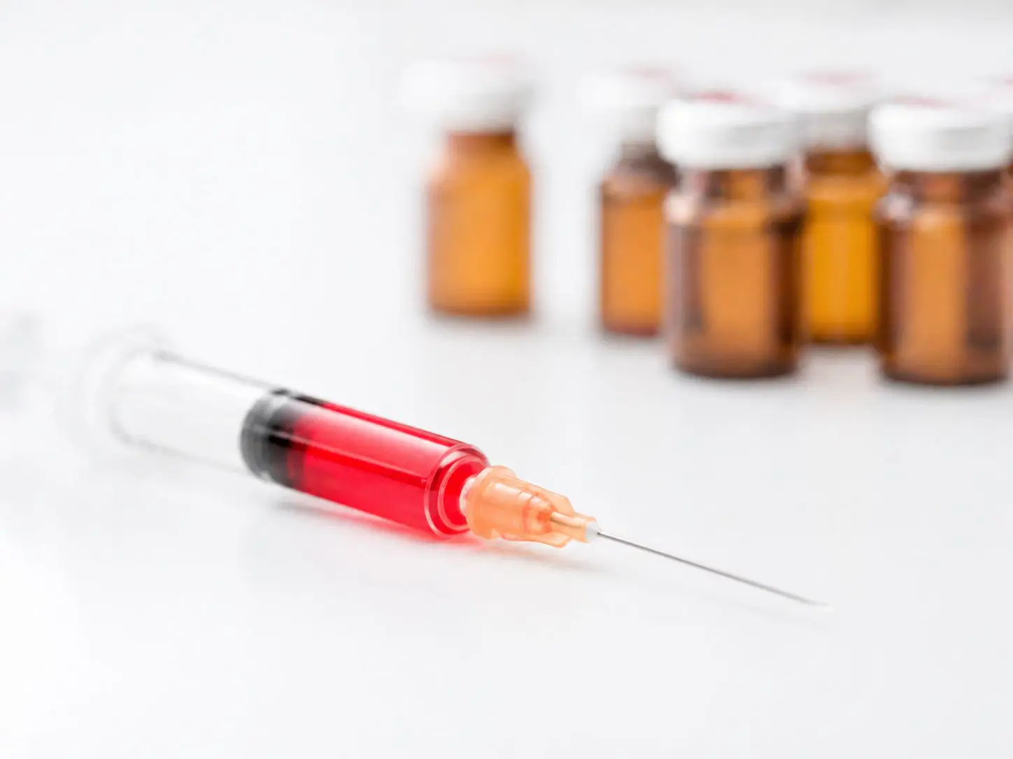 Filled syringe in the foreground with medication vials in the background