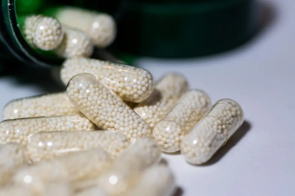 Close-up of supplement capsules filled with small beads spilling from a bottle