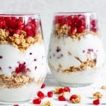 homemade yogurt parfait with granola and pomegranate fruit in glasses on white wooden table. delicious dessert. healthy breakfast