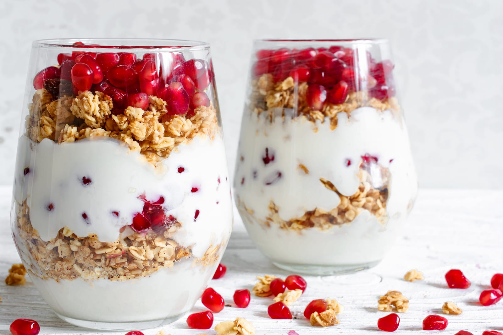 homemade yogurt parfait with granola and pomegranate fruit in glasses on white wooden table. delicious dessert. healthy breakfast