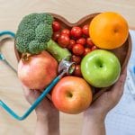 Diabetes monitor, Cholesterol diet and healthy food eating nutritional concept with clean fruits in nutritionist's heart dish and patient's blood sugar control record with diabetic measuring tool kit
