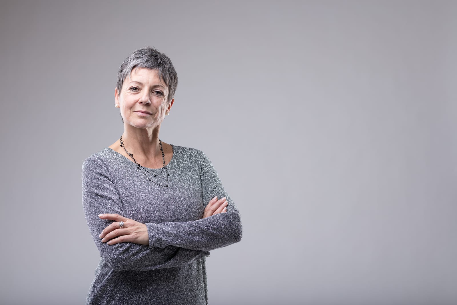 Smiling happy older woman with short hair giving the camera a beaming friendly smile isolated on grey