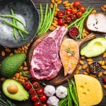 A healthy balanced diet of red meat, fatty fish, and other healthy options are laid out in an appetizing arrangement on a wooden table.