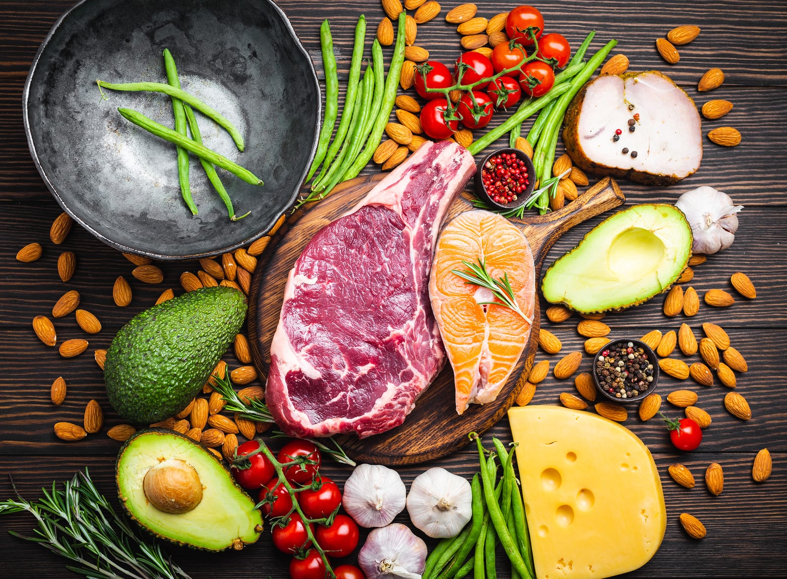 A healthy balanced diet of red meat, fatty fish, and other healthy options are laid out in an appetizing arrangement on a wooden table.