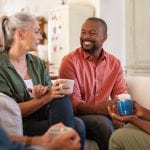 A group of happy older adults sit drinking coffee in a social get-together.